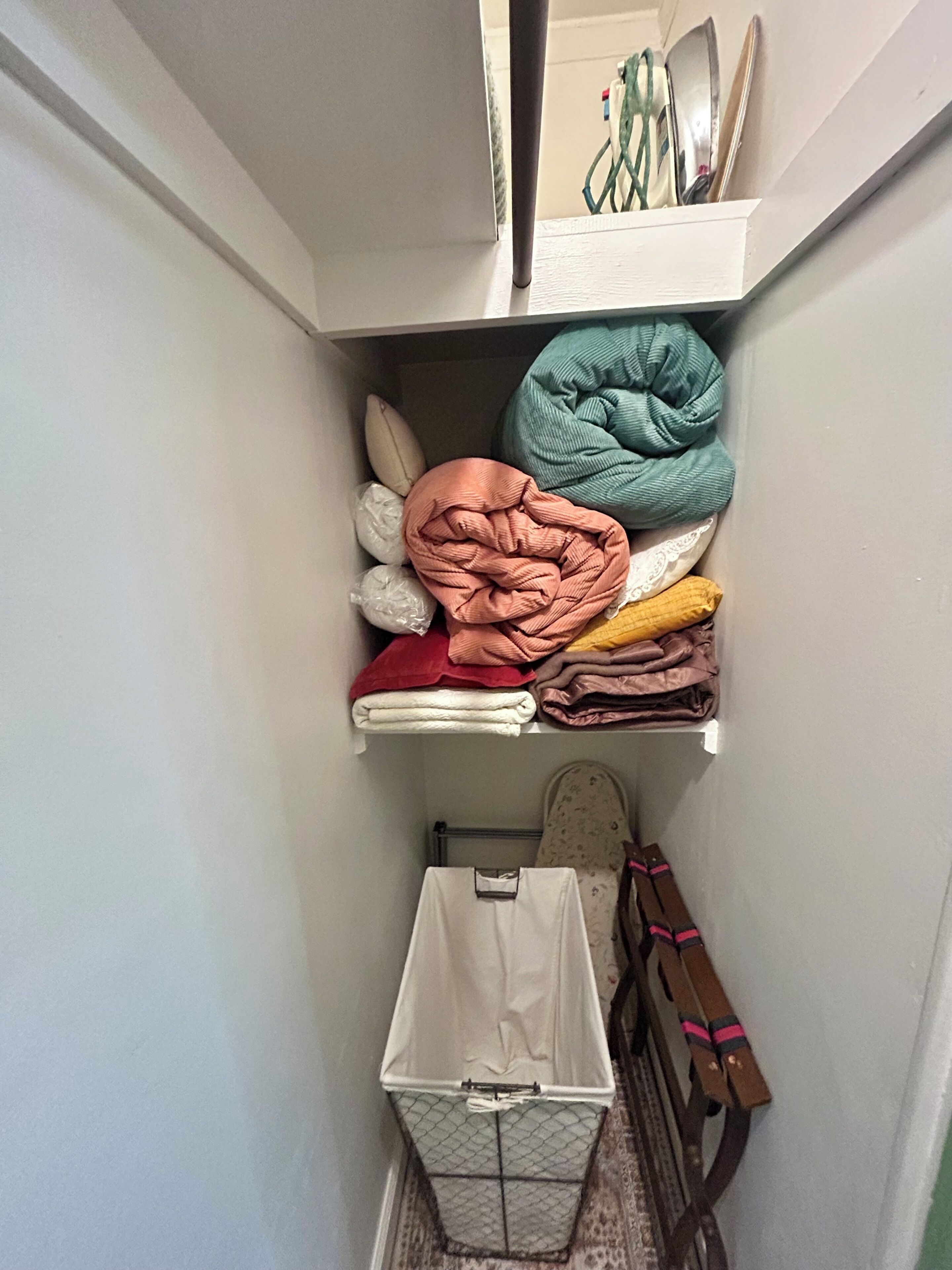 Een inpandige kast met planken vol opgevouwen handdoeken en een opbergbox.