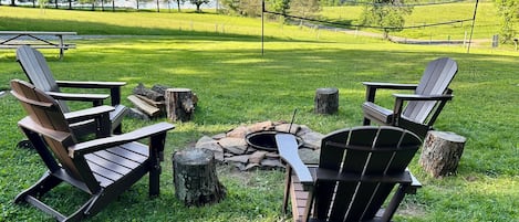 Ein Rasenbereich im Freien mit Adirondack-Stühlen und einer Feuerstelle.