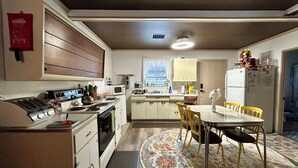 Une cuisine compacte équipée d’une cuisinière, d’un four à micro-ondes et d’un réfrigérateur. On y trouve une table à manger avec des chaises et un tapis.