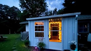 Une petite maison de plain-pied avec un porche, une porte d’entrée et une fenêtre décorée de guirlandes lumineuses.