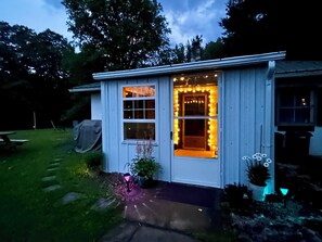 Una casa pequeña de un solo piso con un porche, una puerta principal y una ventana adornada con luces de cuerda.