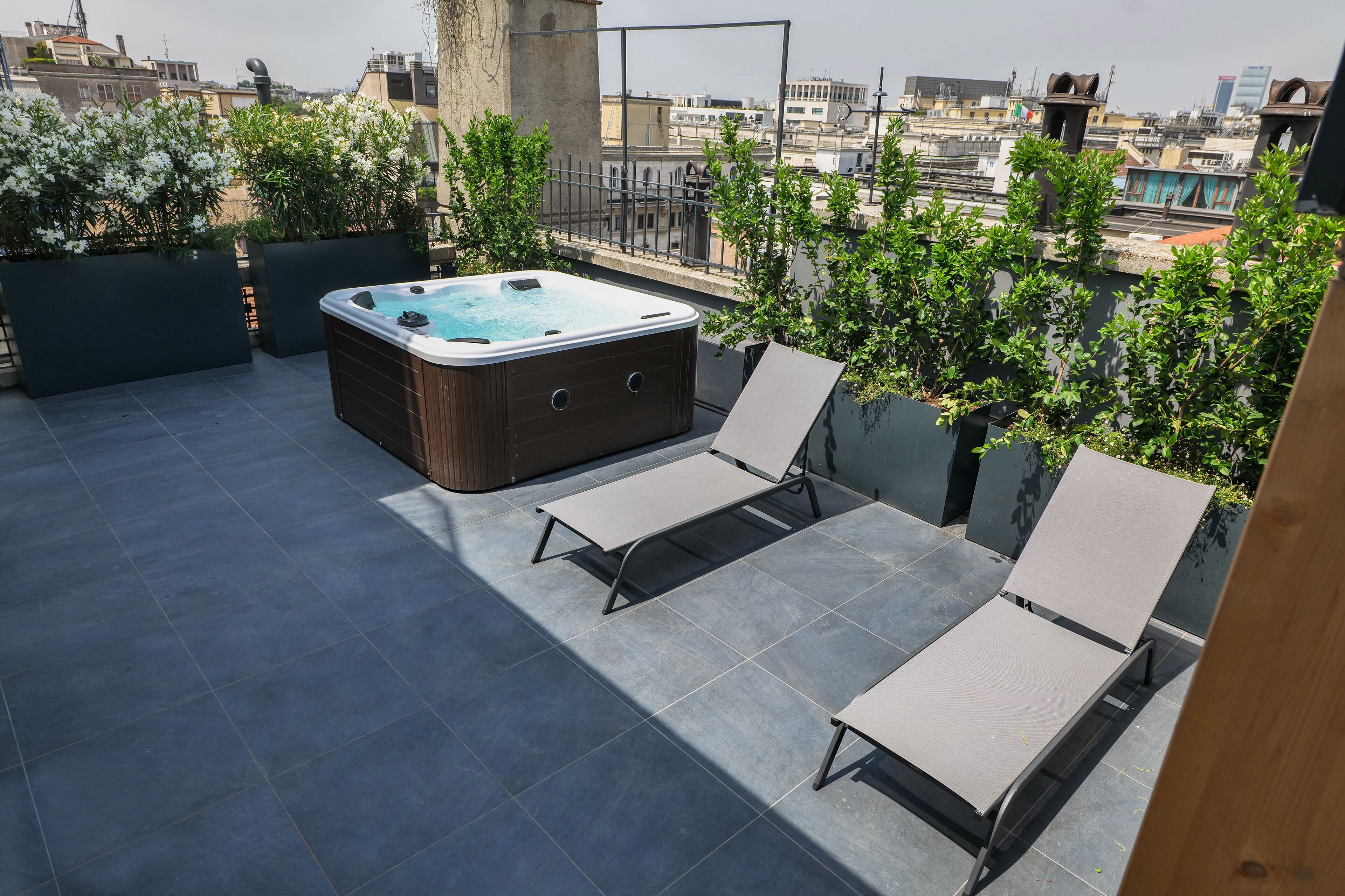 A rooftop terrace with a hot tub, two lounge chairs, and potted plants.