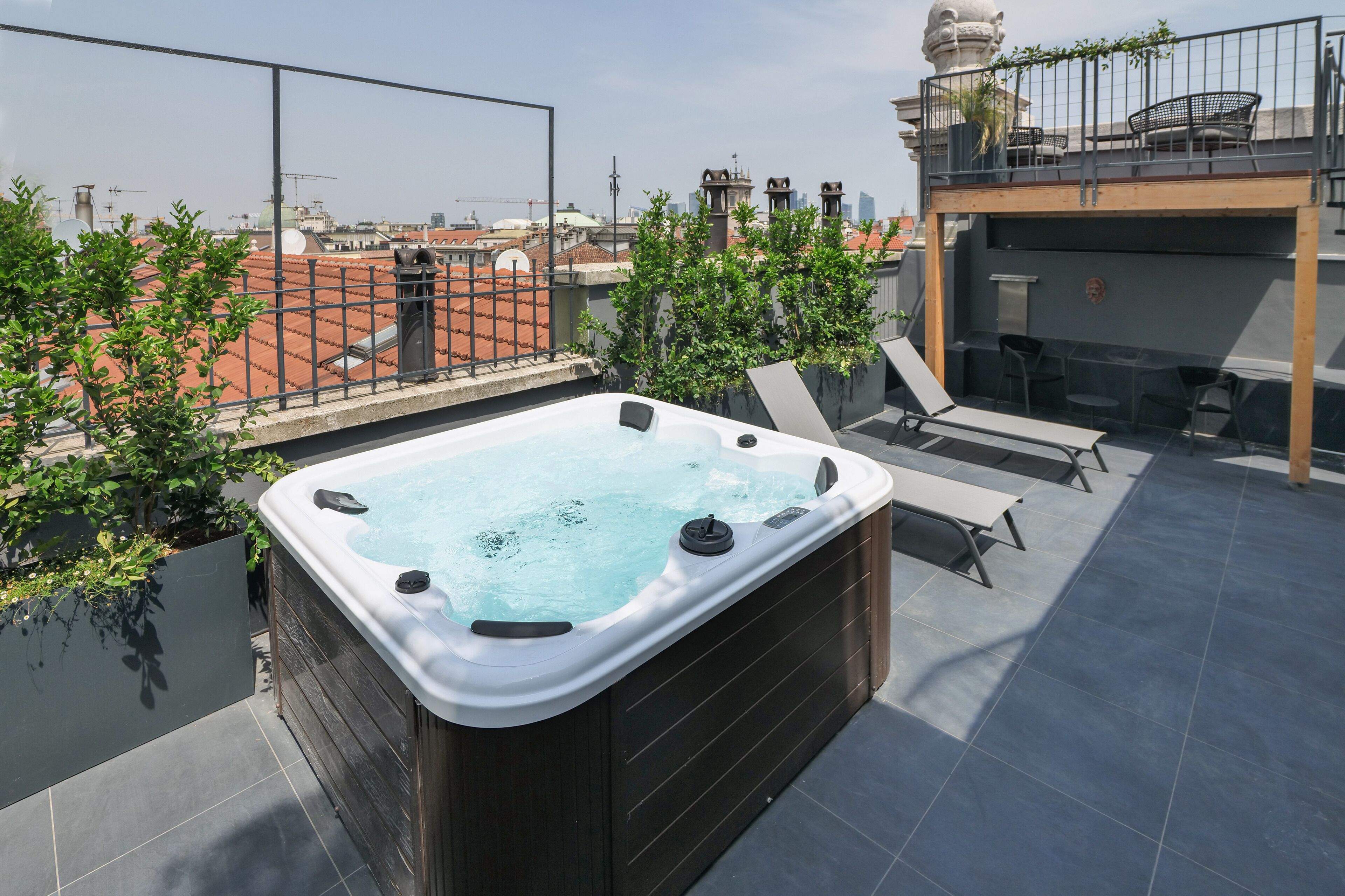A rooftop terrace with a hot tub, lounge chairs, and a view of the cityscape.