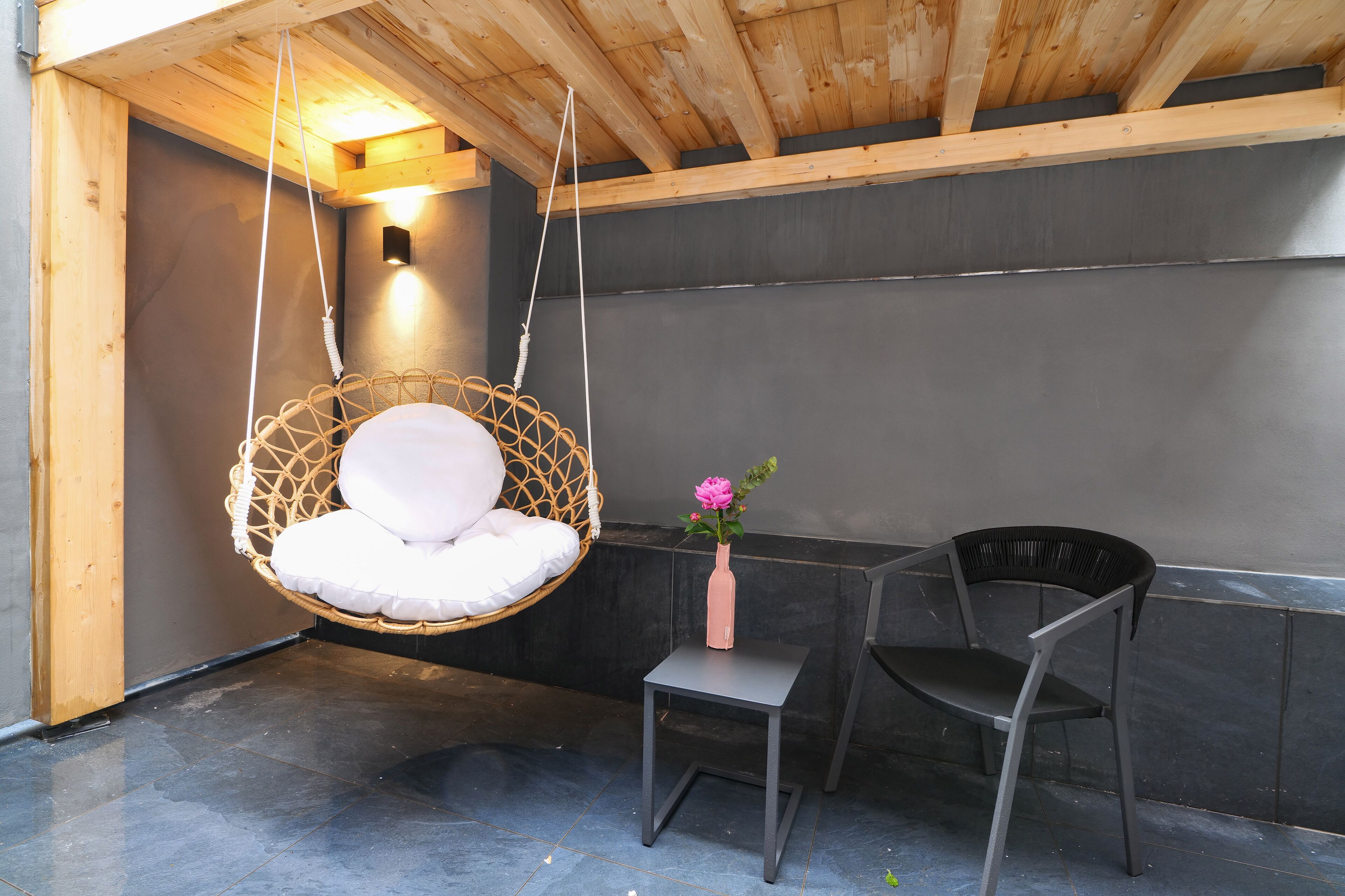 Una habitación con una silla colgante, una mesita con un florero y una silla.