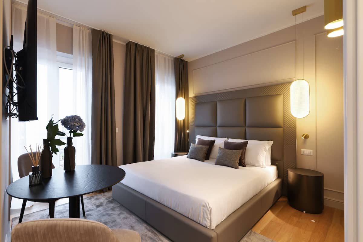 Una habitació d'hotel moderna amb un llit gran, una taula rodona amb un vas i espelmes, i un televisor muntat a la paret.