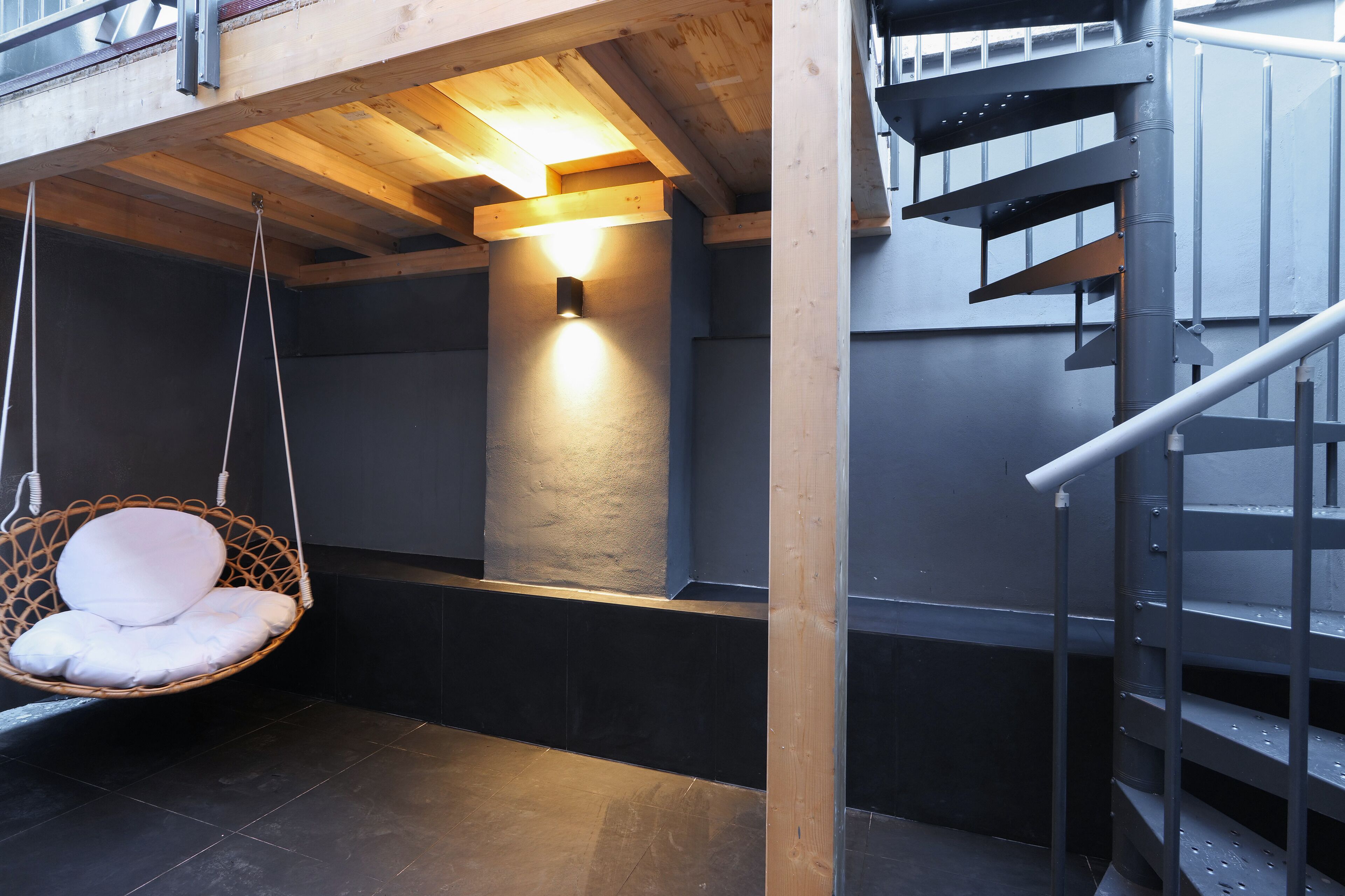 A hanging chair with a cushion, a wall-mounted light, and a metal staircase.