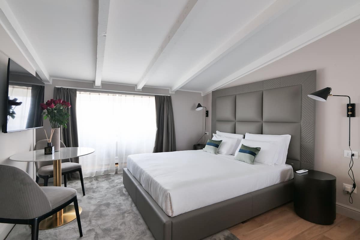 Habitació d'hotel moderna amb un llit gran, una taula rodona per dinar, una cadira, un escriptori i una televisió penjada a la paret.