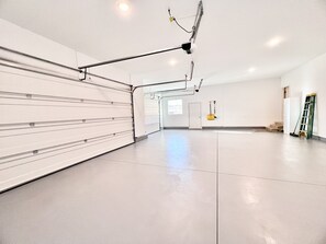 A spacious, well-lit room with a large white door, a broom leaning against the wall, and a ladder propped up.