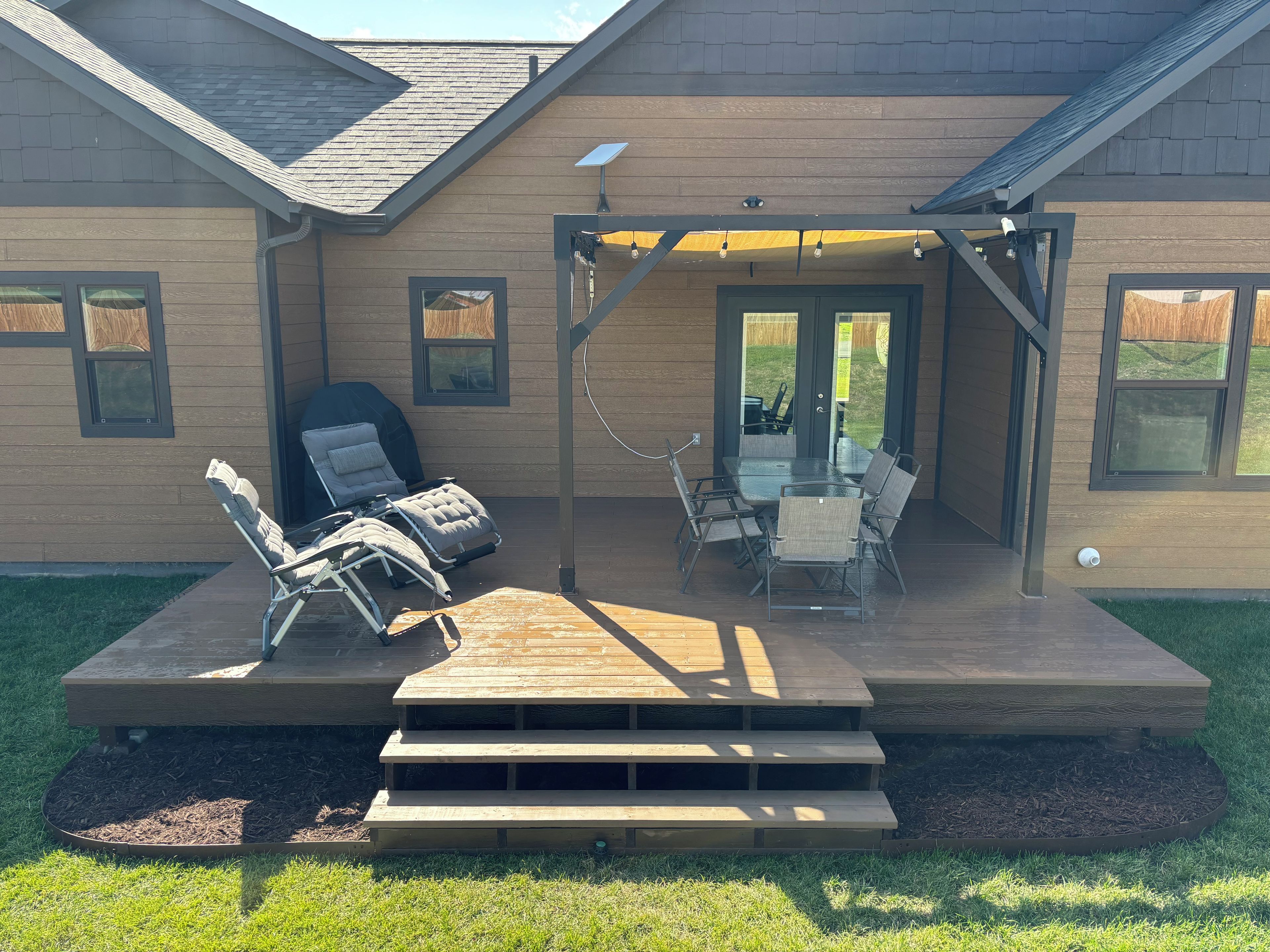 A covered patio with outdoor furniture, a grill, and a wooden deck.