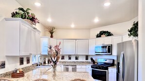 A modern kitchen with white cabinets, a granite countertop, a stainless steel refrigerator, and wooden chairs. - New home, close to skiing, hunting, rodeos, hiking. Fenced yard, pet friendly. (Darby)