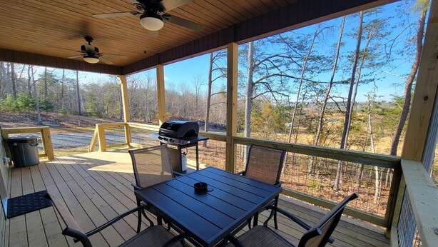 A covered outdoor deck with a table, chairs, a grill, and a trash can. - New cabin- access to horse trails, Pilot Mtn & Hanging Rock St. Pks (Pinnacle)