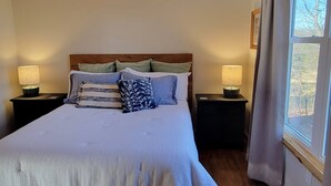A bedroom with a large bed, wooden headboard, two bedside tables with lamps, a ceiling fan, and a window with curtains. - New cabin- access to horse trails, Pilot Mtn & Hanging Rock St. Pks (Pinnacle)