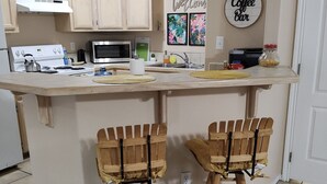 A kitchen with a central island, two wooden bar stools, a microwave, a stove, and a coffee bar sign.