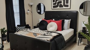 A modern bedroom with a black upholstered bed, a patterned rug, and a ceiling fan.