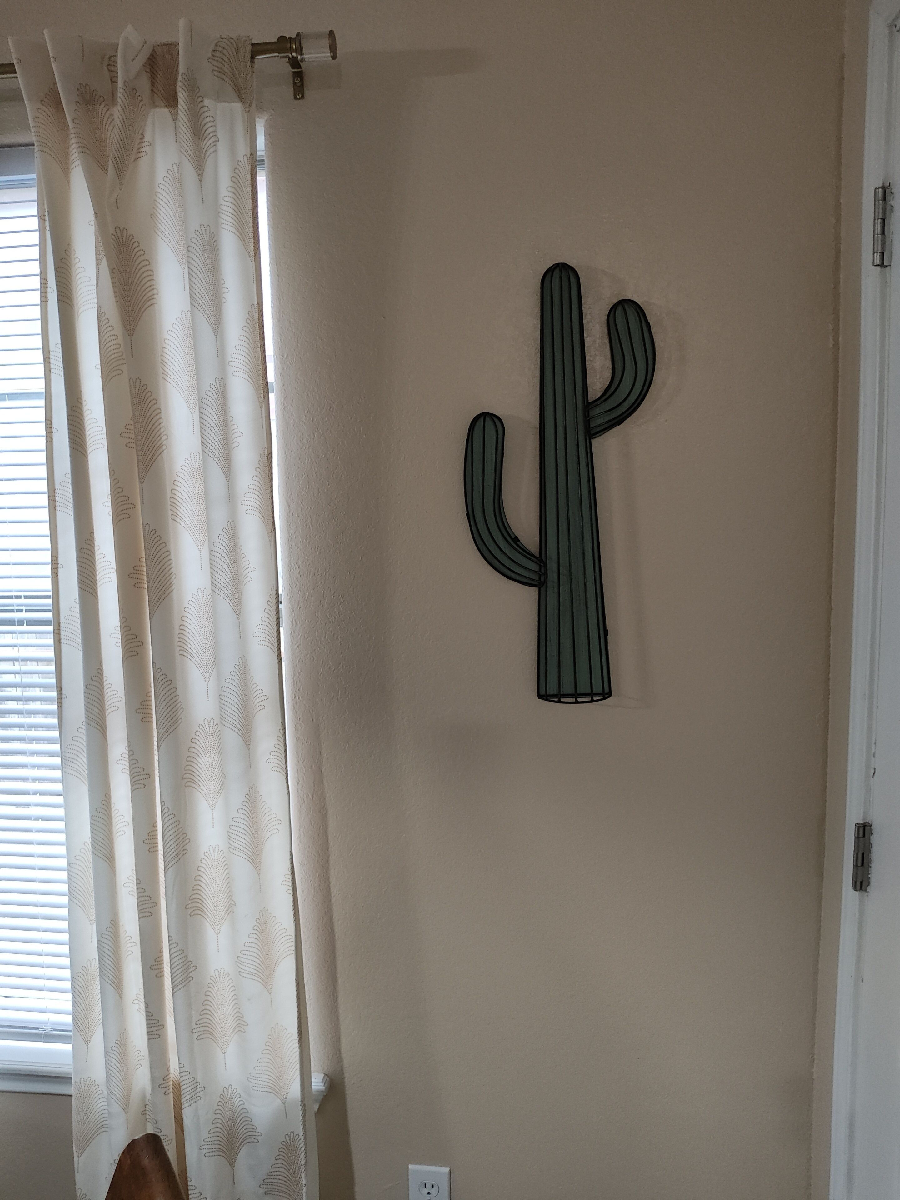 A room with a window, a cactus decoration on the wall, and a curtain with a leaf pattern.