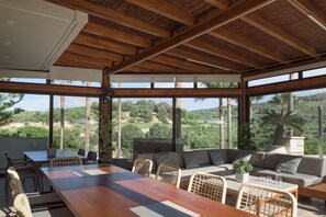An open-plan living area with a wooden ceiling, large windows, a dining table, and a sofa.