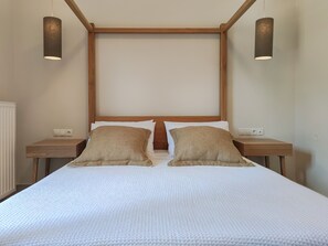 Ein ordentlich bezogenes Bett mit zwei Kissen, einem Holz-Kopfteil und Nachttischen mit Lampen.