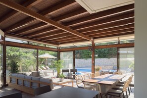 Eine überdachte Terrasse mit Pool, Sitzgelegenheit im Freien und großen Fenstern.