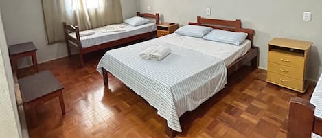 A room with two beds, a ceiling fan, a painting on the wall, and a wooden floor.