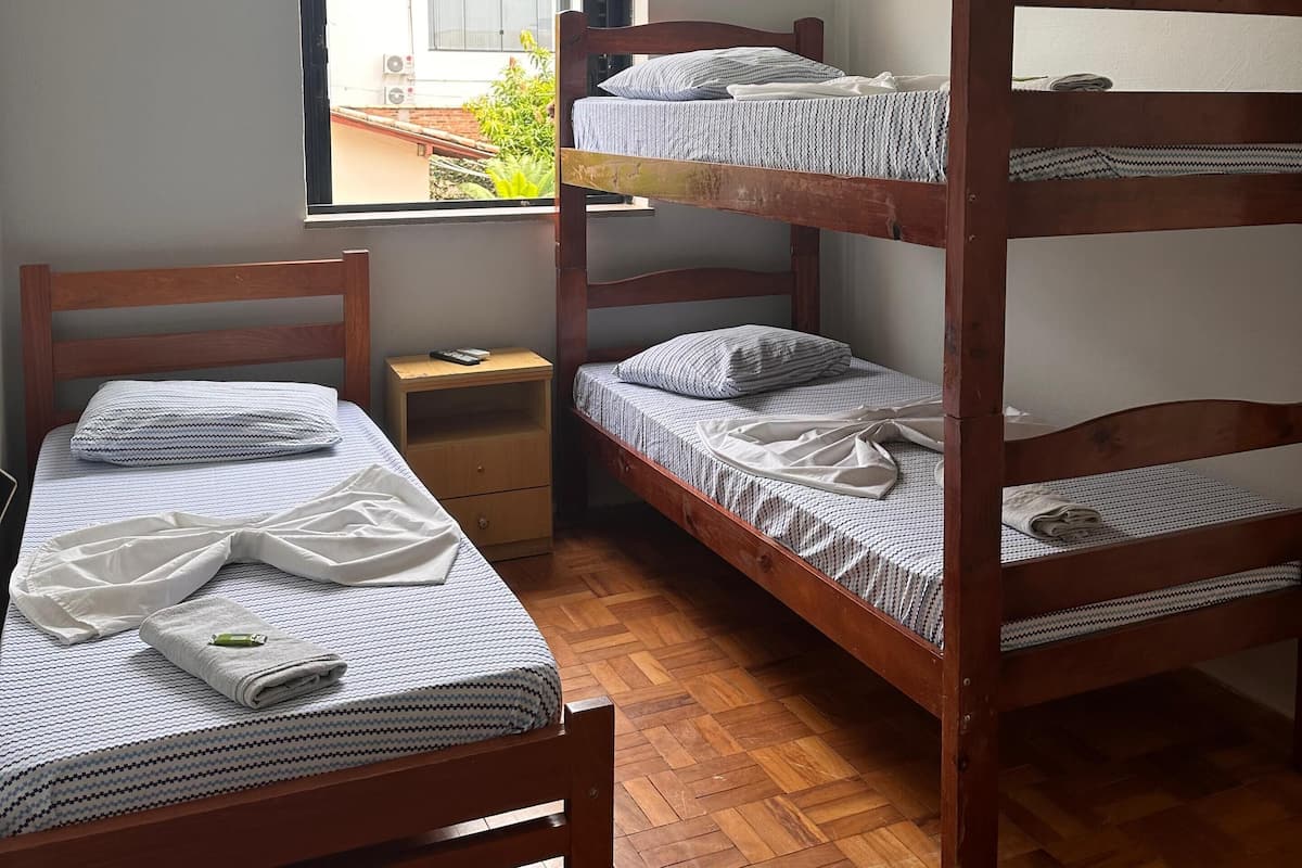 Une chambre de dortoir équipée de lits superposés, d’un bureau, d’une chaise, d’une fenêtre donnant sur des bâtiments et d’un appareil de climatisation.