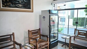 A seating area with wooden benches, a refrigerator with a glass door, and a framed picture on the wall. - Hotel Bandeirantes (Sao Joao da Boa Vista)