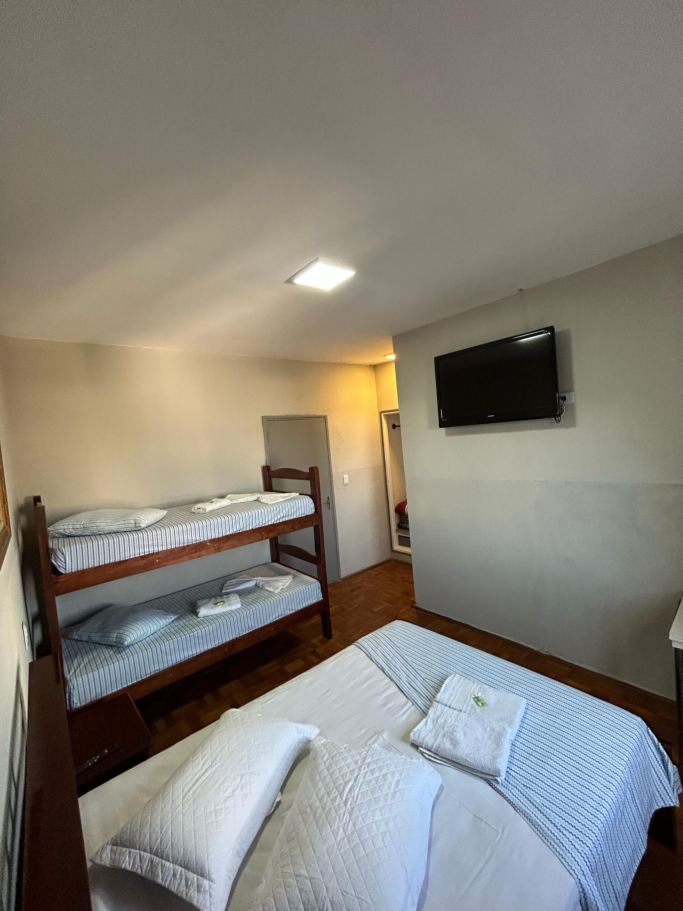 Una habitación con literas, un televisor de pantalla plana montado en la pared y una puerta que da a otra habitación.