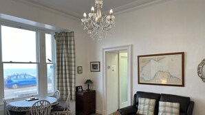 A living room with a dining area, a chandelier, a map on the wall, and a view of the sea through the window. - Stunning location - beachfront ground floor flat with private parking. Fab views (North Berwick)