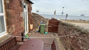 A patio area with a table and chairs, a brick wall, a wooden gate, and a view of the sea. - Stunning location - beachfront ground floor flat with private parking. Fab views (North Berwick)
