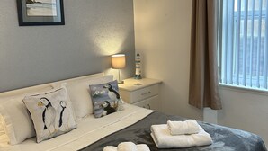A neatly made bed with a grey blanket and two rolled towels, a bedside lamp, a framed picture on the wall, and a window with blinds. - Stunning location - beachfront ground floor flat with private parking. Fab views (North Berwick)