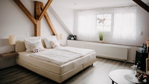 A bedroom with a bed, bedside tables, a window with curtains, a radiator, and a small table with a plant. - Altstadt-Residenz Manz (Wachenheim an der Weinstrasse)