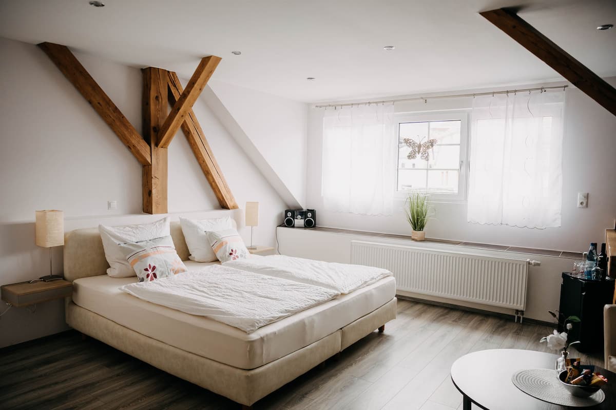A bedroom with a bed, bedside tables, a window with curtains, a radiator, and a small table with a plant.