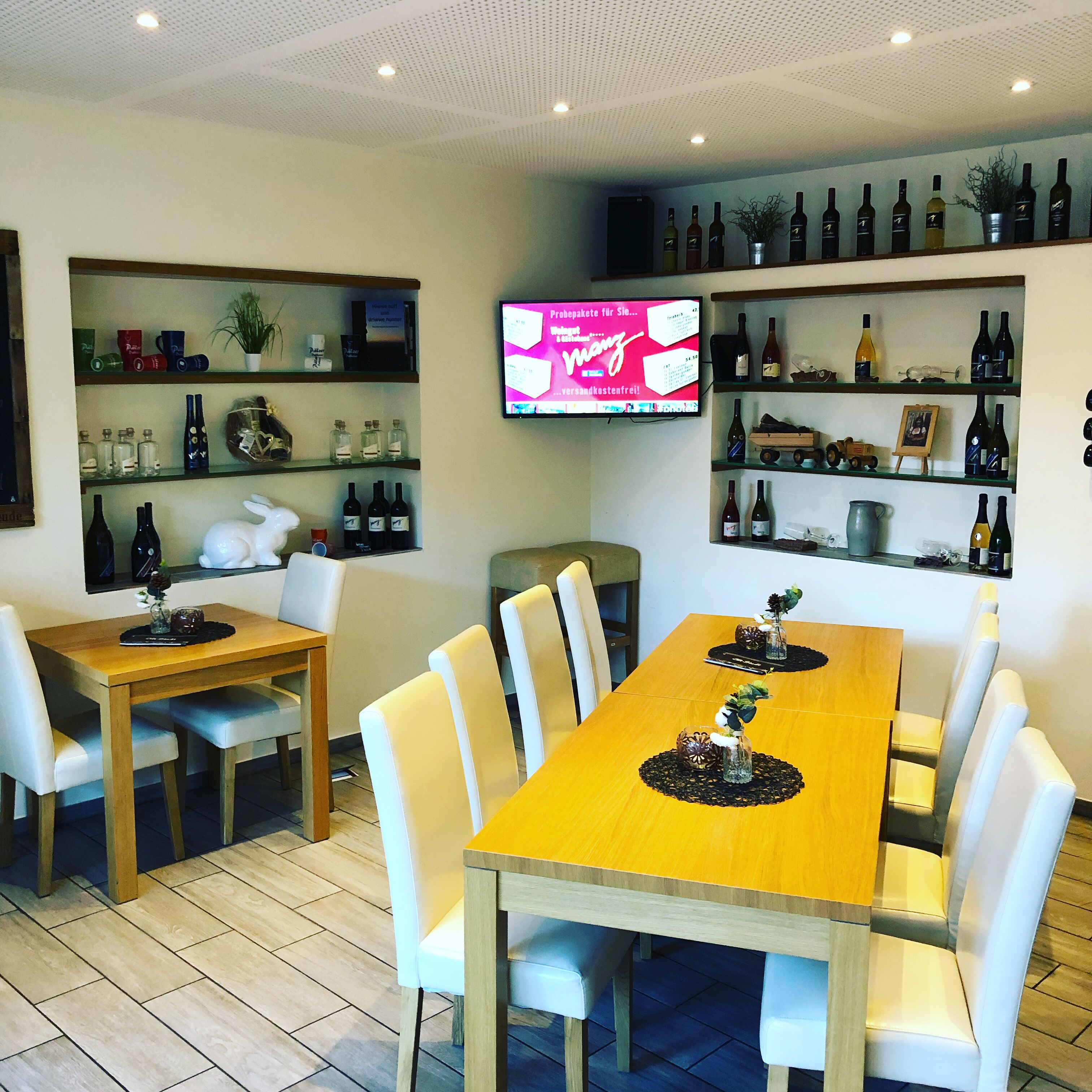 Un restaurante con una mesa de comedor de madera, sillas blancas y estantes con botellas de vino.