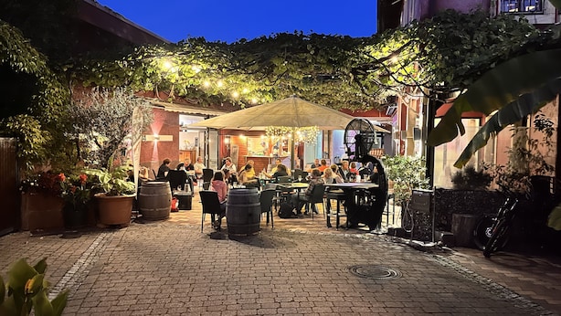 An outdoor dining area with tables and chairs, surrounded by potted plants and a brick wall. - Altstadt-Residenz Manz (Wachenheim an der Weinstrasse)