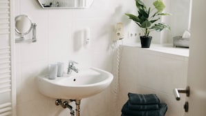 A bathroom with a white sink, a round mirror, a potted plant, and a towel on a stool. - Altstadt-Residenz Manz (Wachenheim an der Weinstrasse)