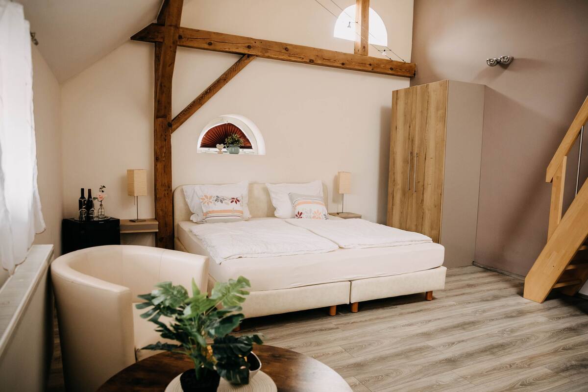 A bedroom with a bed, a wooden ceiling, a window, a plant, and a staircase.