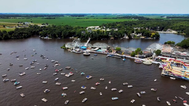 Un río con numerosos barcos y un parque con atracciones y noria.