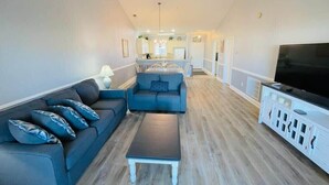 A spacious living room with a dark blue sofa, a coffee table, and a TV on a white cabinet. - Amazing Pond View condo + pool at MyrtleWoods (Myrtle Beach)