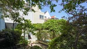 Un bâtiment blanc doté d’un toit en pente, entouré d’une végétation luxuriante et agrémenté d’un petit jardin avec un banc.