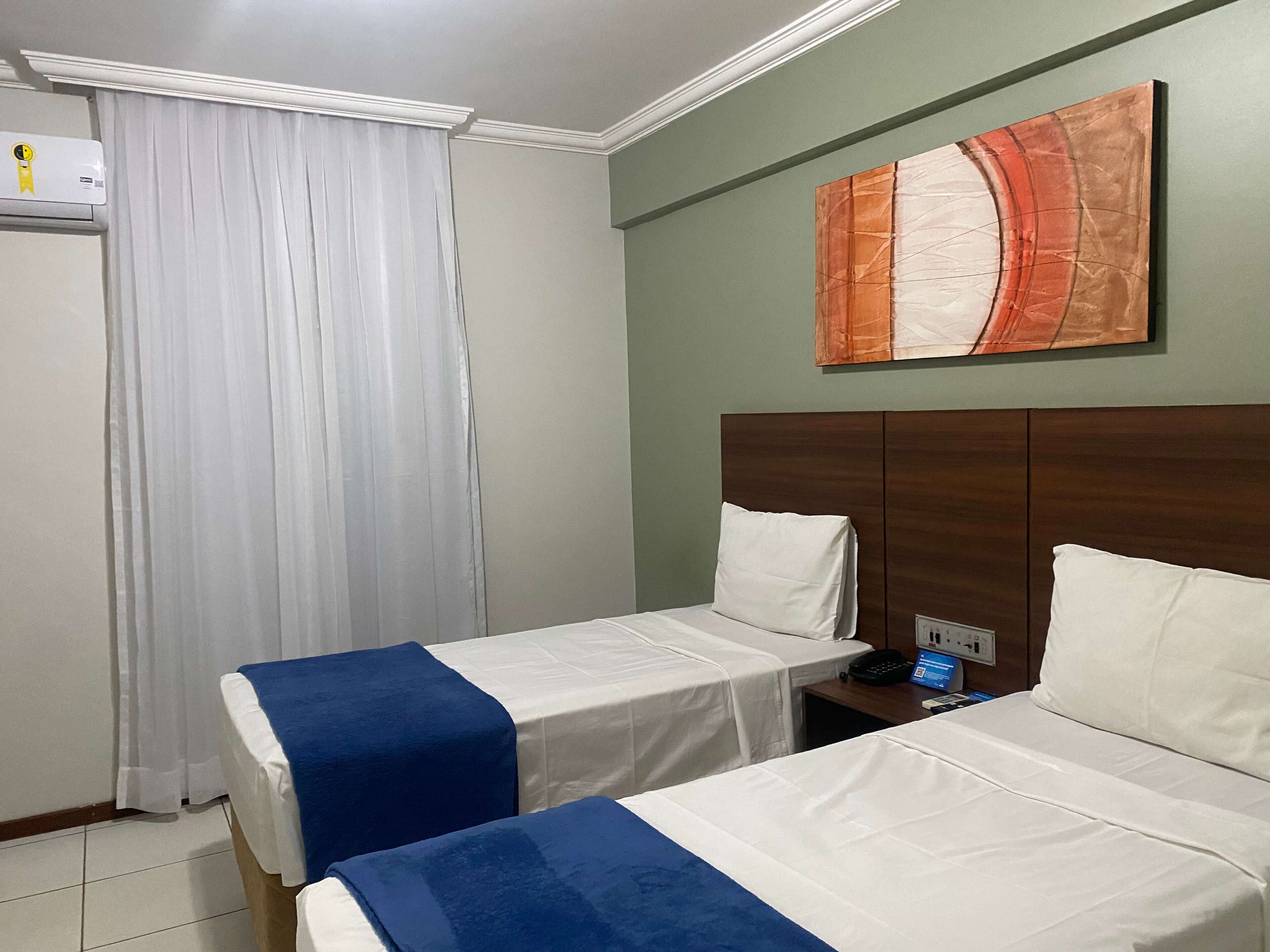 A hotel room with two beds, a wooden headboard, a painting on the wall, a telephone, and a power outlet.