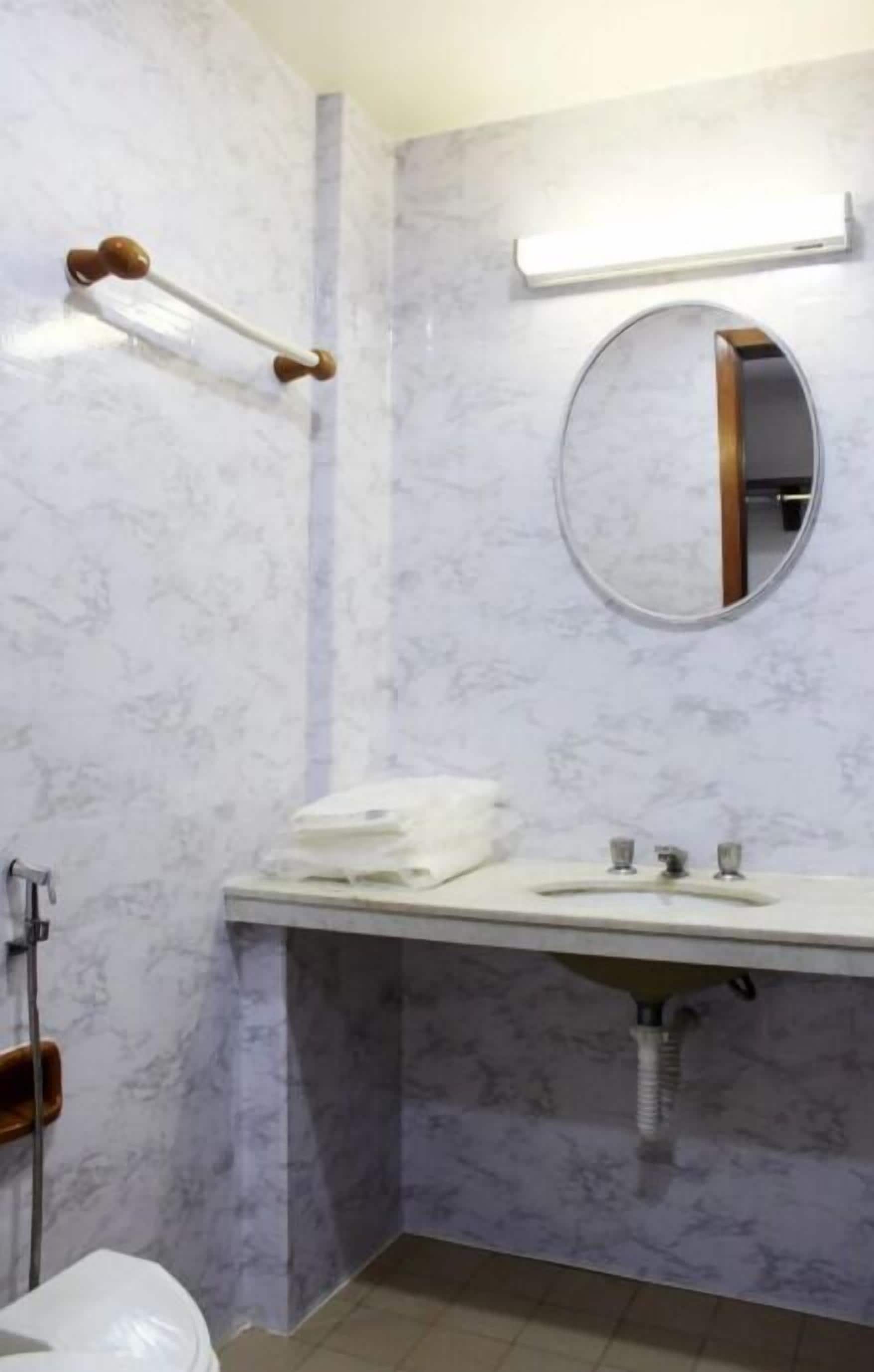 Un baño con pared de mármol, un espejo redondo, un lavamanos blanco y un perchero para toallas.