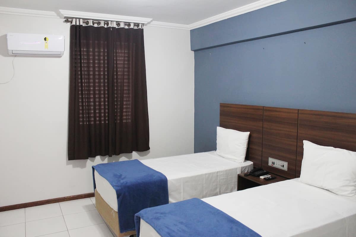 Une chambre d’hôtel avec deux lits simples, une table de chevet avec un téléphone et une télécommande, et un appareil de climatisation fixé au mur.
