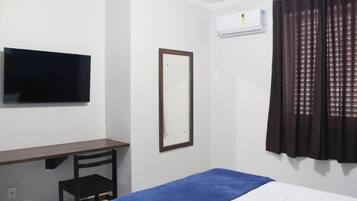 Quarto de hotel com cama, escrivaninha, cadeira, televisão, espelho e janela com cortinas.