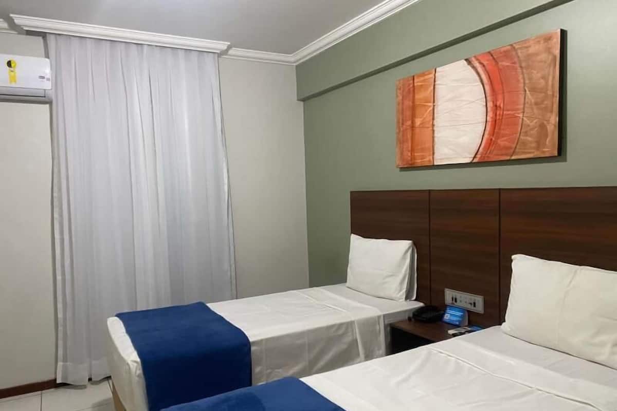 Une chambre d’hôtel avec deux lits, une table de chevet, un tableau au mur et une fenêtre avec des rideaux.