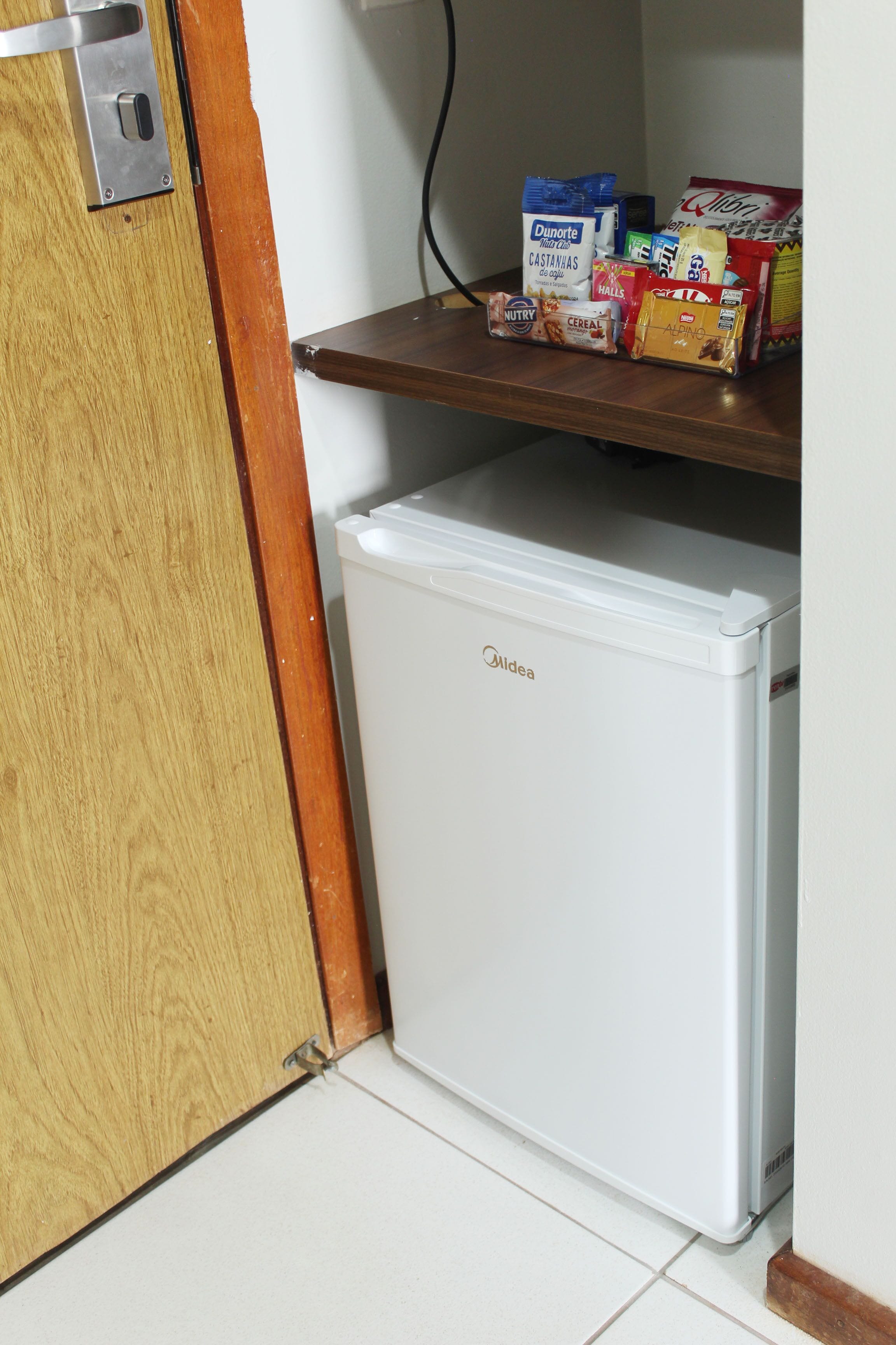Ein kleiner Kühlschrank mit Holztür und einem darüberliegenden Regal, das verschiedene Lebensmittel beherbergt.