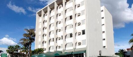 A multi-story hotel with a central entrance, parking area, and a sign indicating the hotel name.