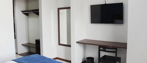 Habitación de hotel con cama, escritorio, silla, televisión y espejo.