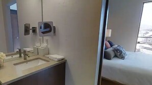 Ett hotellrum med badrum som har handfat, spegel och handduksdispenser.