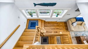 Una escalera de madera conduce a un dormitorio en el altillo, con un ventanal grande y una decoración de pez.