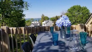 Una mesa al aire libre con cristalería azul y un jarrón de flores, frente a una valla de madera con vistas a casas y árboles.