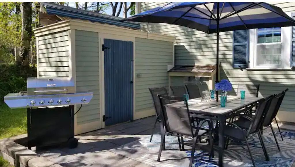 An outdoor patio with a grill, dining table, chairs, and a blue umbrella.